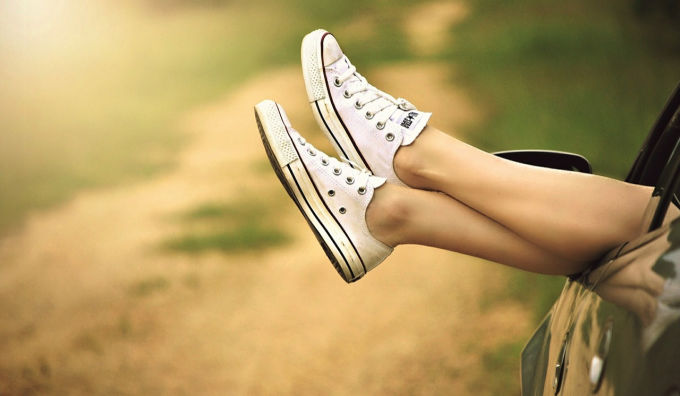 Womans legs with sneakers out car window enjoying summer
