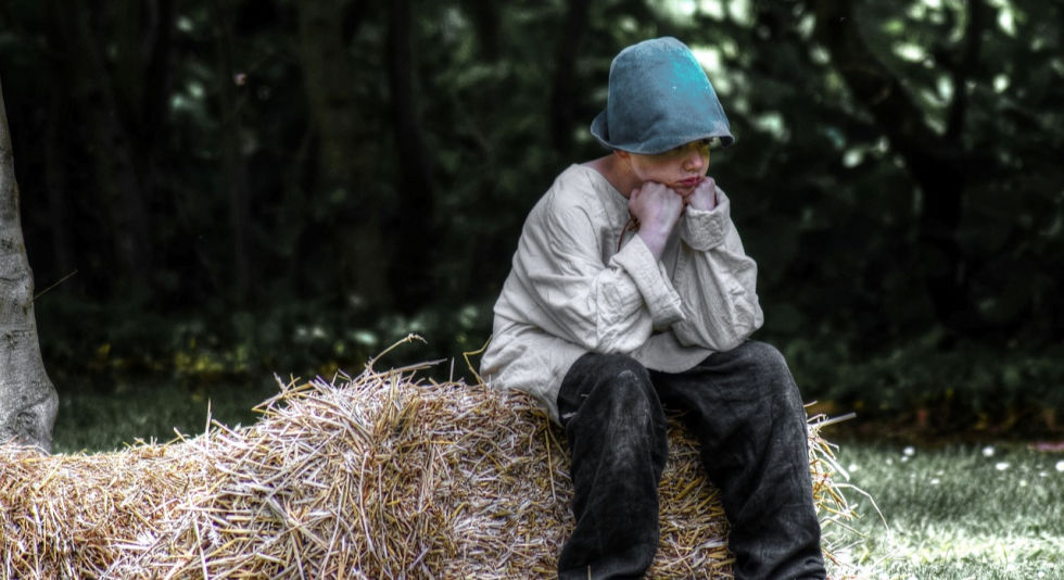Boy in blue cap sitting on hay bale looking upset. How to use constructive criticism rather than destructive.