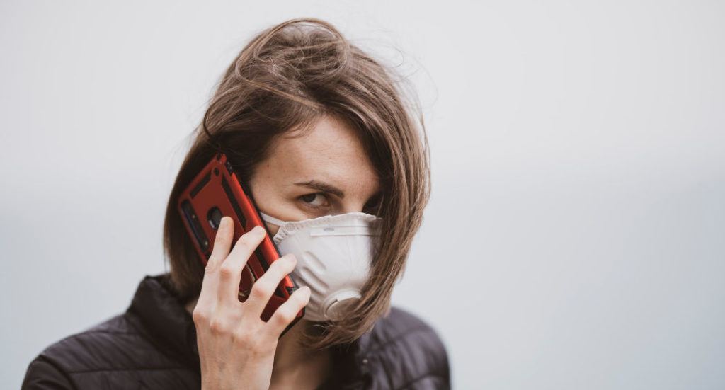 image of woman using cell phone wearing face mask N95 looking directly into the camera lens