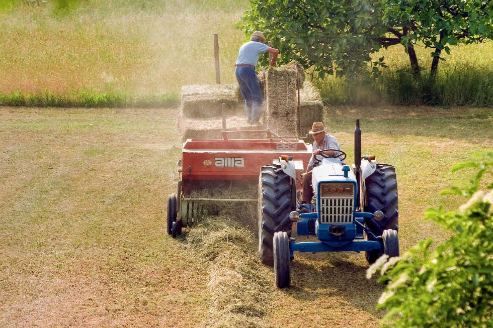 Farmer baling hay on open tractor with man on the trailer stacking bales. Why rural America is conservative.