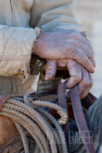 Worn male hands resting on the saddle horse holding a horse's bridle reins. God is in control.
