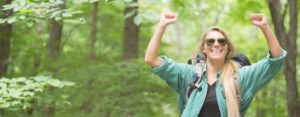 woman hiking in the woods, hands raised in victory. Turn Up the Flame on Lukewarm Passions or Deflated Dreams