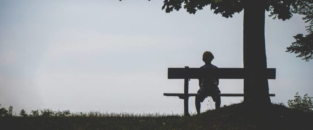 boy on a bench alone under a tree with vast sky