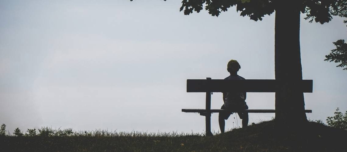 boy on a bench alone under a tree with vast sky